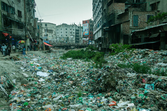 Dhaka, Bangladesh - 15 June 2026: View of a heavily polluted canal filled with plastic waste and debris near the Buriganga River, surrounded by dense urban buildings and local residents.