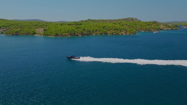 Aerial drone footage of a fast speedboat racing across the Adriatic Sea in Croatia, with the camera smoothly tracking its movement as it speeds past lush islands, leaving a dramatic white wake.