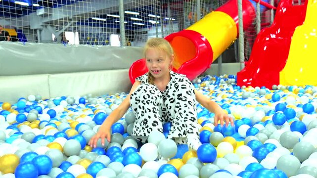 Cute little girl playing and throwing plastic balls in colorful dry ball pit at indoor playground
