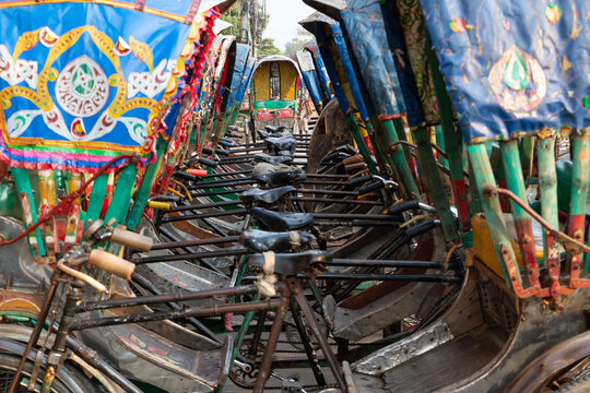 Dhaka, Bangladesh - 17 May 2024: View of a row of colorful cycle rickshaws parked on a city street, featuring vibrant hand-painted hoods and traditional metal frames.