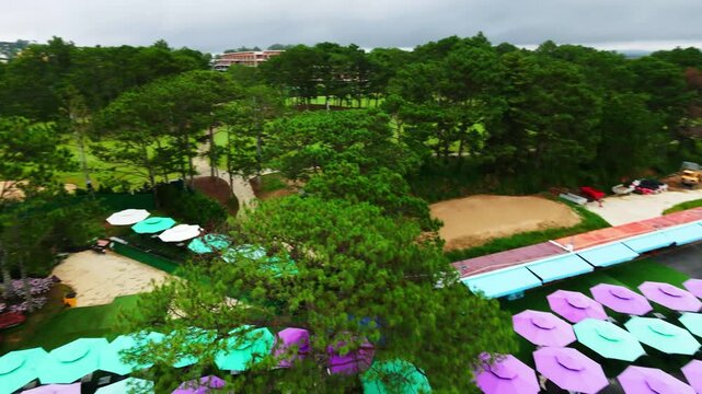 Aerial view of colorful umbrella display in garden surrounded by trees on cloudy day