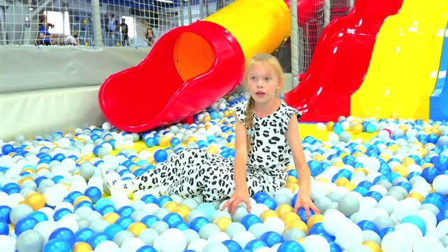 Cute little girl playing and throwing plastic balls in colorful dry ball pit at indoor playground