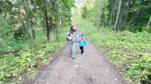 A mother and young son walk along a forest path at Valaam on Lake Ladoga. Tall green trees surround them in the tranquil woods.