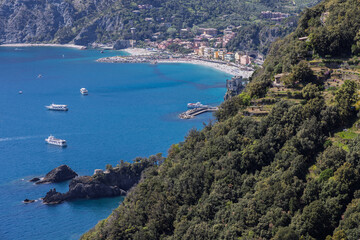 Naklejka premium Monterosso al Mare in northwest Italy highlights green slope framing town and passenger boats in strong afternoon sunlight.