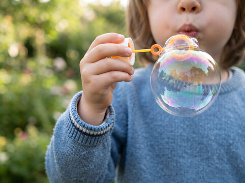 Child blowing large colorful bubble outdoors