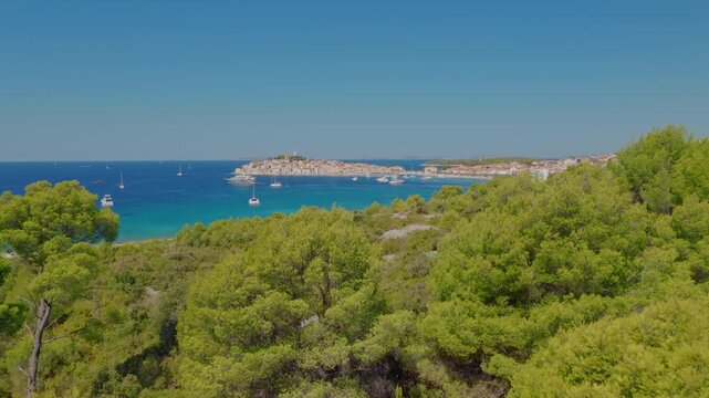Aerial drone view of Primo&scaron;ten, Croatia, with a smooth forward reveal movement through Mediterranean vegetation, gradually unveiling the historic town, turquoise Adriatic Sea, boats and coastline.