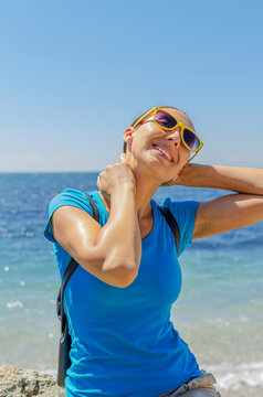 A happy woman wearing yellow sunglasses relaxes by the blue sea on a sunny day.