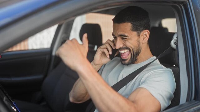 Man hispanic young in car talking on smartphone, smiling with raised hand and seatbelt fastened while parked by street; happiness connection.