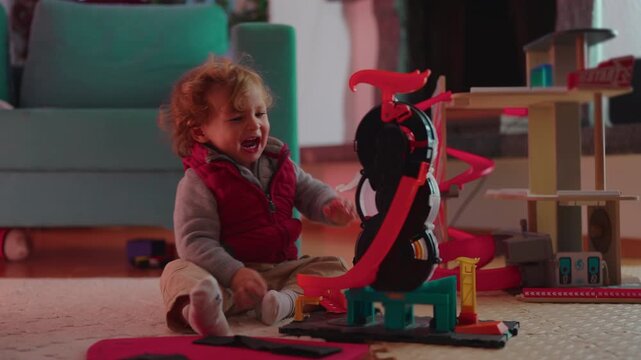 Frustrated toddler pulls at an action playset on the living room floor but cannot remove a stuck toy, expressing persistence, problem solving and emotional development
