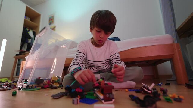 Focused school-age boy modifies a detailed brick model while seated on his bedroom floor, developing persistence, design awareness and creative independence