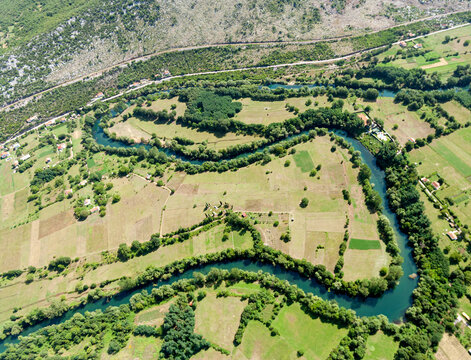 Aerial view of the meandering Zeta River flowing through lush green fields and rural landscapes in Danilovgrad, Danilovgrad Municipal, Montenegro.