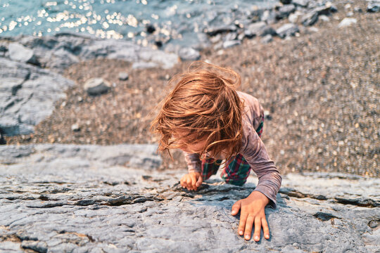 Close-up of a boy climbing a boulder with hands gripping rock