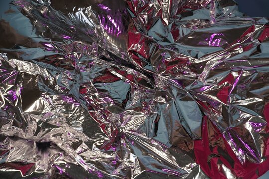 Crumpled aluminum foil with purple-pink reflections. Shiny metallic texture, lots of folds, silver and neon highlights, abstract background, close-up.