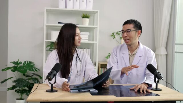 Asian male and female doctors holding an X-ray film, discussing medical diagnosis during a healthcare podcast interview. Recording an educational audio broadcast in a modern clinic studio setting