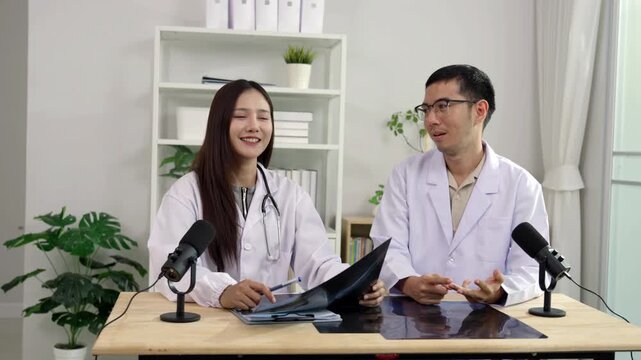Asian male and female doctors holding an X-ray film, discussing medical diagnosis during a healthcare podcast interview. Recording an educational audio broadcast in a modern clinic studio setting