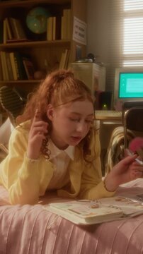 Vertical shot of Caucasian teenage girl lying down, blowing bubble gum and decorating scrapbook, zooming in. Clip is perfect for youth lifestyle and teenage-focused commercial campaigns