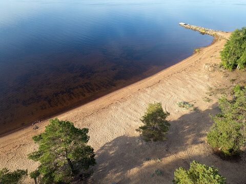 Aerial view of Meriniemi Beach with sandy shoreline, pine trees, and a small stone pier extending into the calm water in Oulu, Pohjois-Pohjanmaa, Finland.