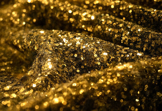 Sparkling golden sequin fabric texture with shimmering light reflections and folds for glamorous fashion design