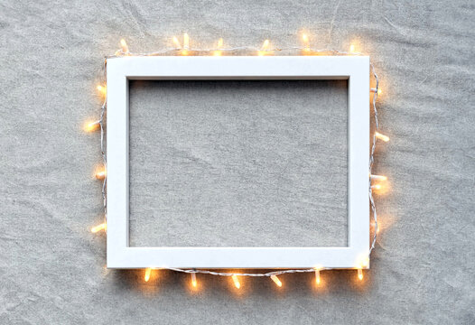 White empty picture frame surrounded by warm glowing string lights on gray background perfect for festive decor