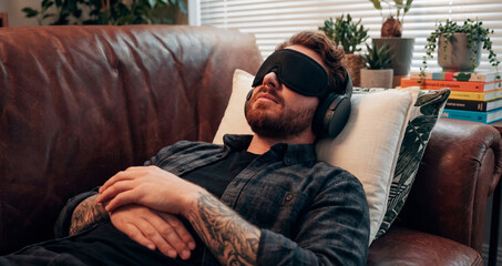 Fototapeta premium Man wearing eye mask and headphones resting and relaxing on a leather couch