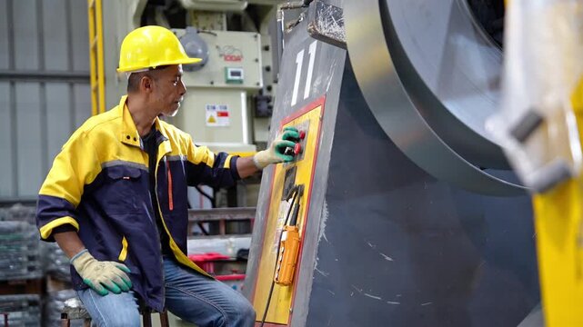 Factory engineer in protective clothing and hard hat operates industrial machinery during production, inspection, quality control, and workplace safety procedures.