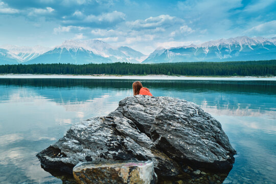 Boy leaning on a boulder at a turquoise lake facing mountains
