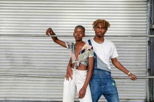 Two individuals pose confidently against a metal shutter backdrop.