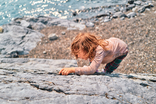 Boy reaching up a boulder face beside a mountain lake