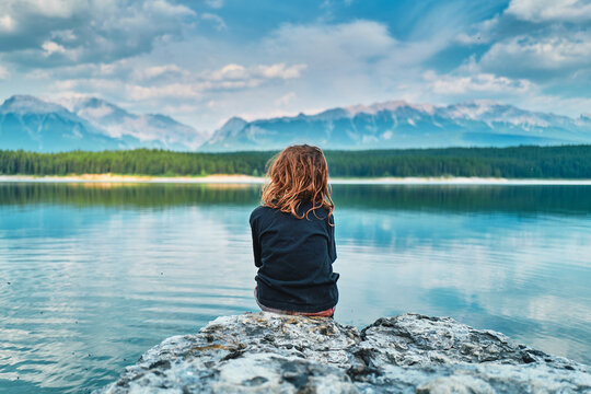 Boy sitting on a rock facing a turquoise mountain lake from behind