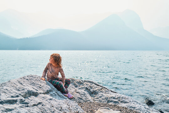 Boy sitting on a rock at a mountain lake looking at hazy peaks