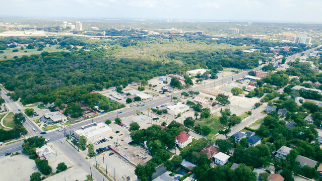 Broadway corridor cuts through Mahncke Park towards Brackenridge Park. Retail storefronts border vehicle parking plazas, neighborhood roadways, green canopy, San Antonio, Texas