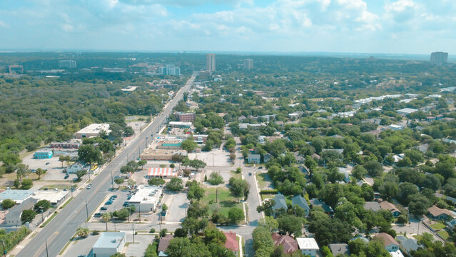 Long thoroughfare intersects Broadway near Mahncke Park residential sector. Mature oaks border single family residences, open retail plazas, sprawling suburban neighborhoods, San Antonio, Texas