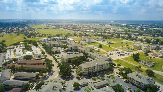 Large residential buildings border open fields near Broadway. Multi family complexes showcase prominent gabled rooflines, extensive surface parking areas, paved community roadways, Texas