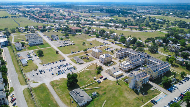 Historic multi wing complex borders expansive open fields near Broadway. Distinct gabled barracks overlook large vehicle lots, access drives, wide sunny lawns, San Antonio, Texas