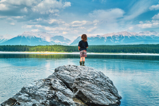Boy standing on a rock facing a turquoise mountain lake from behind