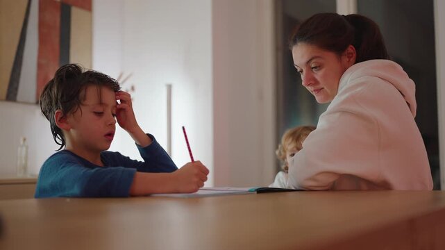 Mother supports son studying at dining table while toddler asks to breastfeed at home, balancing education, nurturing, responsive parenting and attention between siblings