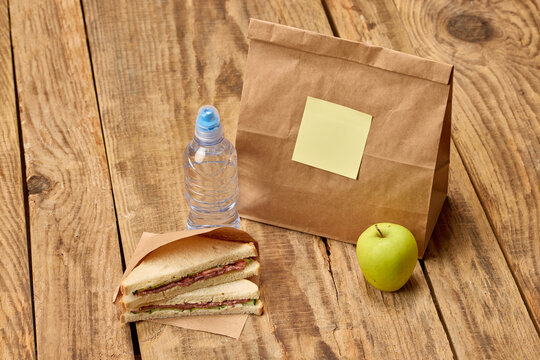 Prepared school lunch with sandwiches, apple, water and paper bag. Concept of homemade meals, student nutrition, parental care and school day preparation.