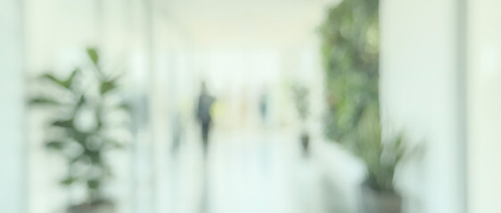 Naklejka premium A softly focused image of a modern office hallway featuring greenery and people walking in a blurred background, conveying a sense of calm and professionalism.