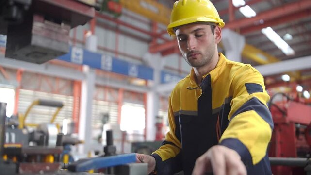 Industrial engineer wearing a safety helmet and protective uniform performs a quality control inspection on machinery in a manufacturing factory.