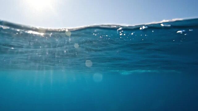 Clear blue ocean water surface split view showing sun reflection above waves while submerged below deep sea level