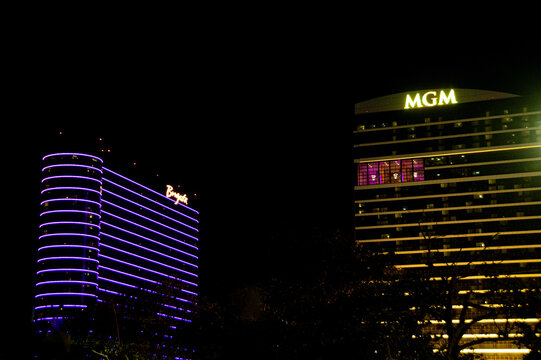 Borgota and MGM hotel and casinos in Atlantic City illuminated at night with purple and gold neon lighting, showing signage and urban nightlife atmosphere. A dramatic exterior shot evoking luxury.
