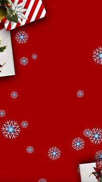Snowflakes falling over christmas wreath decoration and gifts against red background
