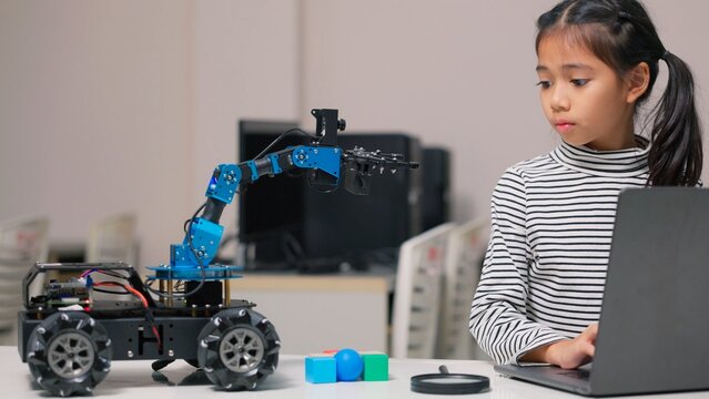 Asian kid pupil happy learning robotics programming and controlling robotic arm in science class. Creative STEM education, future technology innovation, school laboratory and child study concept.