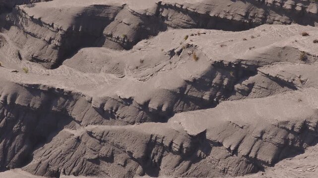 Detailed aerial of smooth gray marl badlands with deep carved channels sparse vegetation and sharp shadows