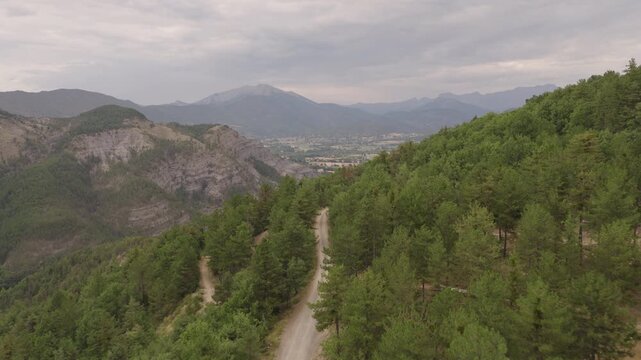 Overlook of green forested ridge gray eroded slopes valley fields and distant mountains under cloudy sky