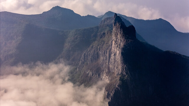 Aerial view of Gunung Kelud rising above a sea of clouds with rugged rocky cliffs and lush green slopes, Kecamatan Ngancar, Jawa Timur, Indonesia.