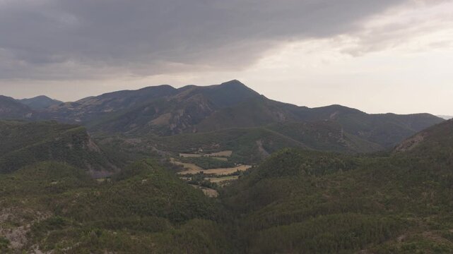 High aerial of rolling green forested mountains open valleys and dramatic cloudy sky over alpine landscape