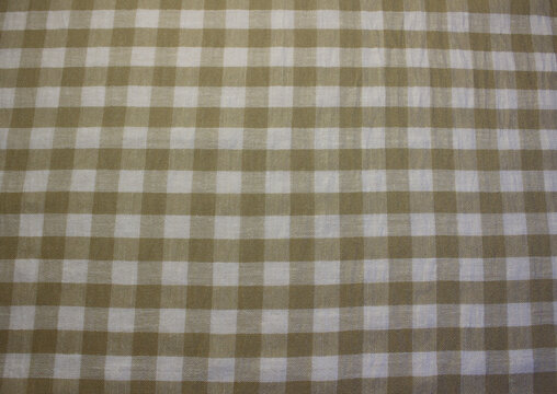 Texture of wrinkled ocher plaid linen like cloth background. Close up of crumpled gold and white gingham fabric. 