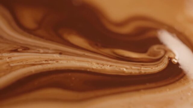 Cream swirling into coffee making artistic patterns in a macro cup shot
