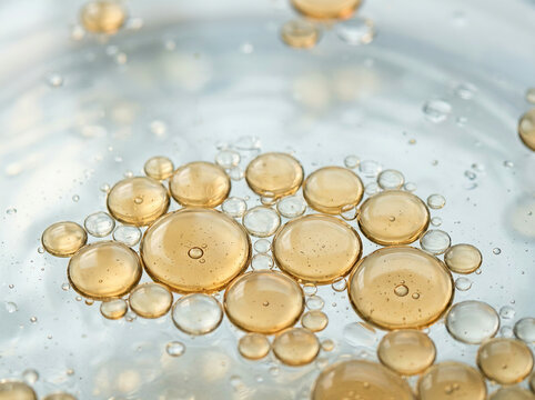 Golden oil droplets suspended in a clear liquid against a soft grey backdrop